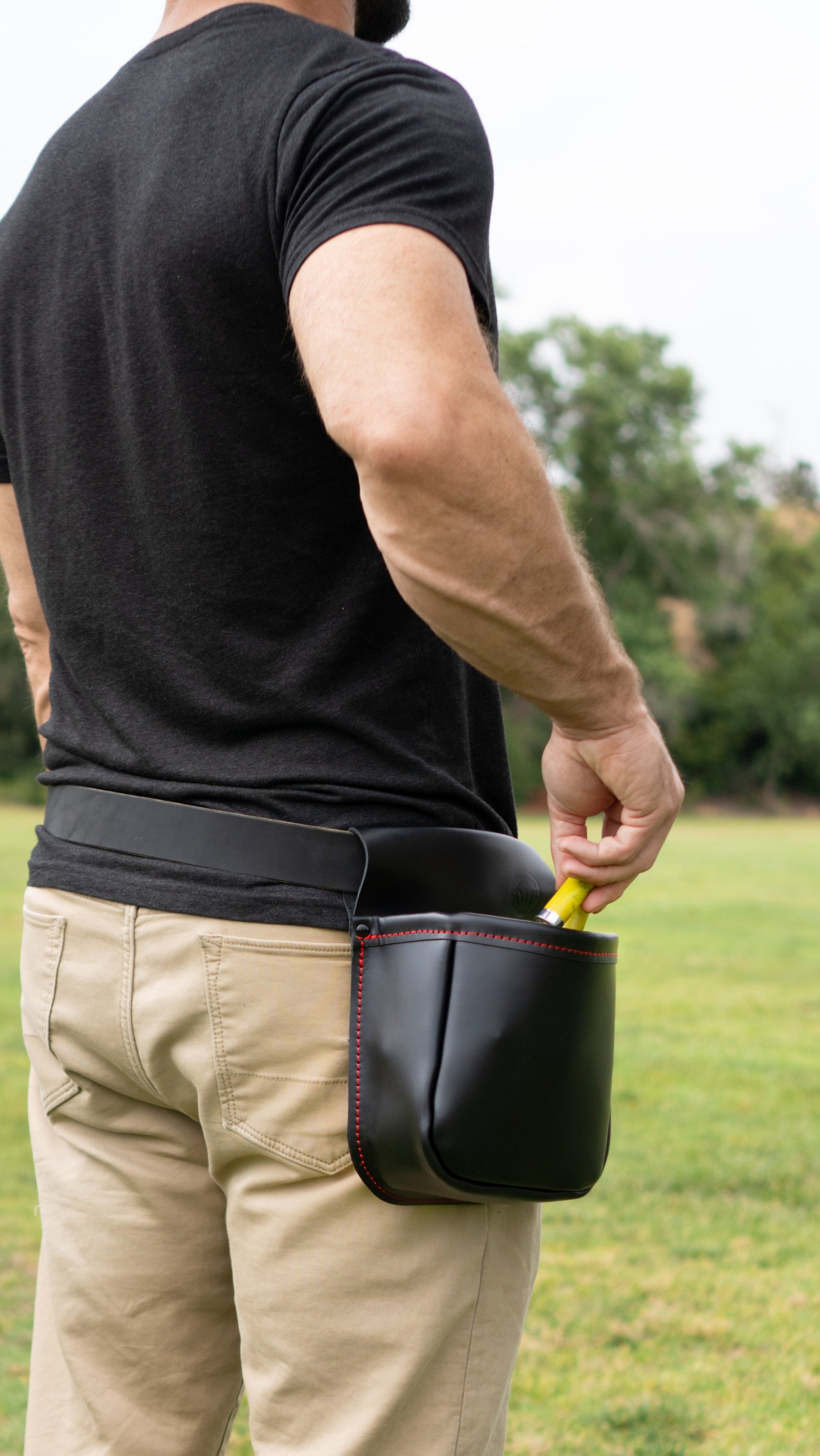 Man standing, pulling shotgun shells from black leather shotgun shell pouch with red stitching on his right hip