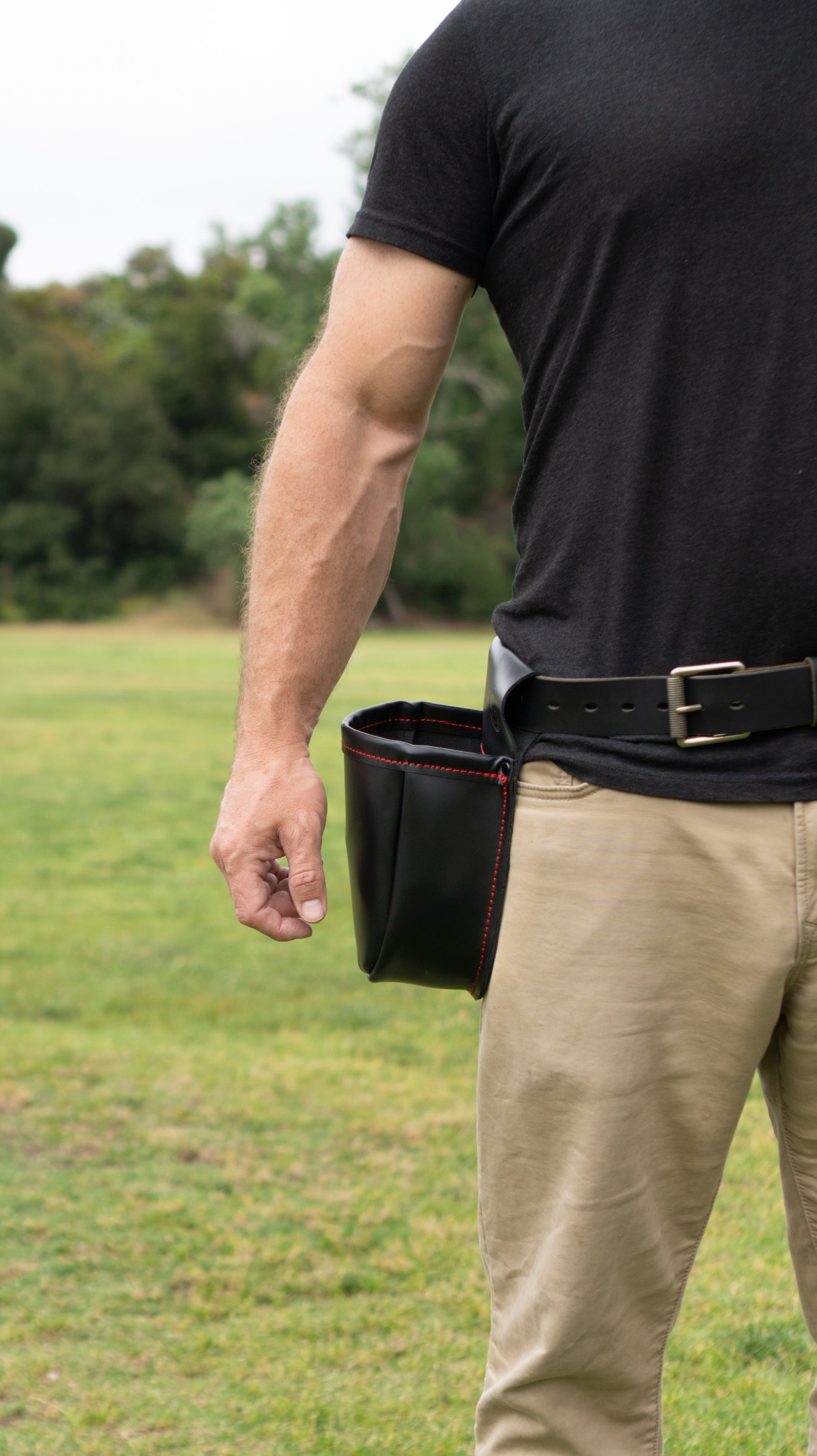 Man standing with a black leather shotgun shell pouch with red stitching on his right hip with arm next to it
