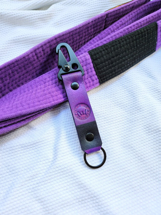 Handmade full grain leather Brazilian Jiu Jitsu purple belt ranked keychain laying with a matching jiu jitsu purple belt and go