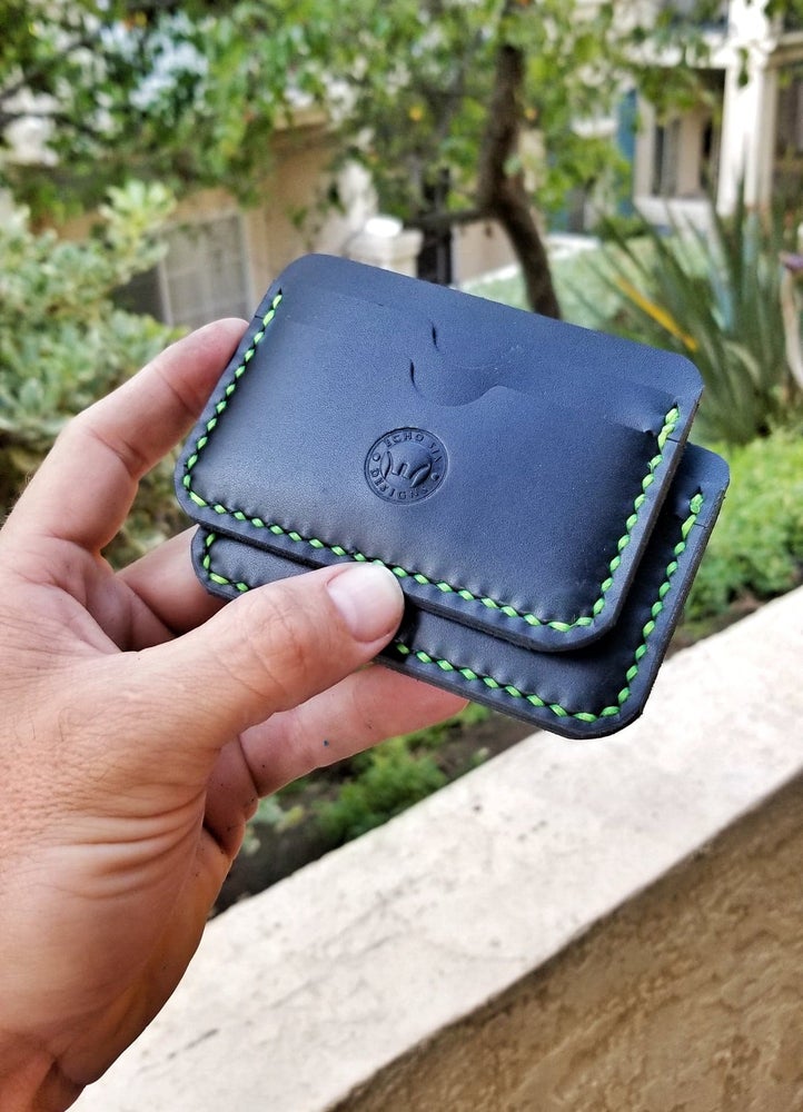 Handmade black full grain leather 5 pocket slim wallet, a stylish and compact accessory for organizing cards and cash with green stitching being held in the hand