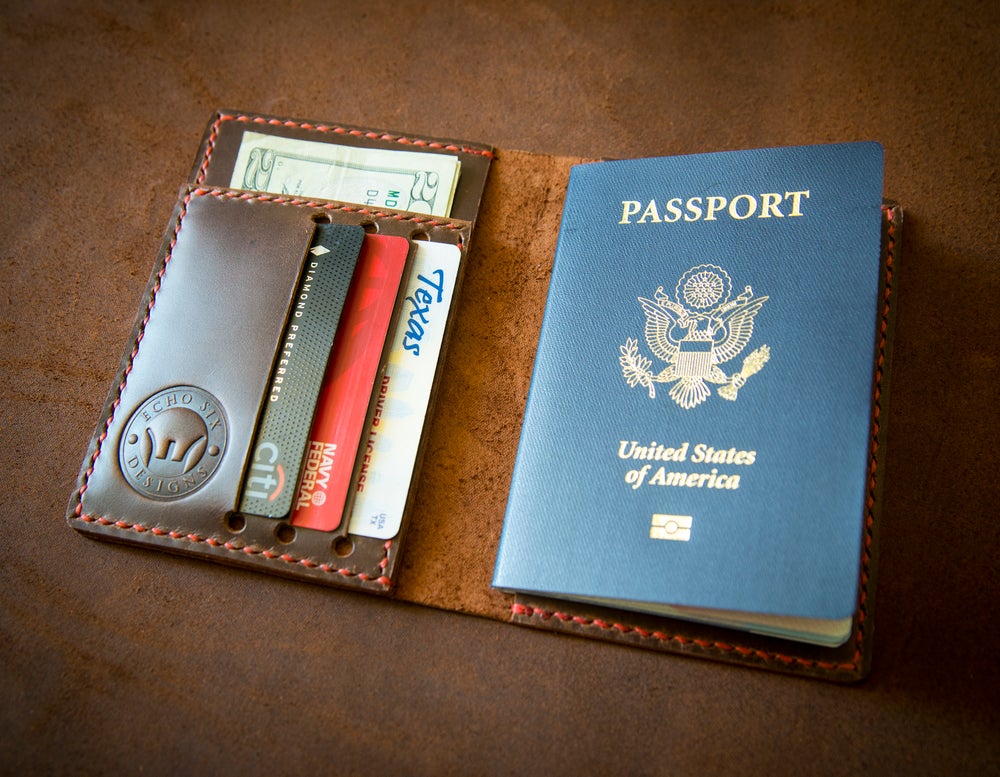Polished brown leather passport wallet stitched with red thread holding a passport and credit cards